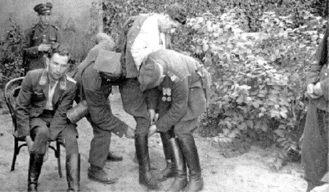 Тот самый эпизод со сниманием сапога с раненого. Кажется, речь идет скорее об обыске, а не об осмотре подбитой конечности. В охране - польские военнослужащие и полицейский (в круглой фуражке). Узнаваем бравый капрал с медалями с первого фото.