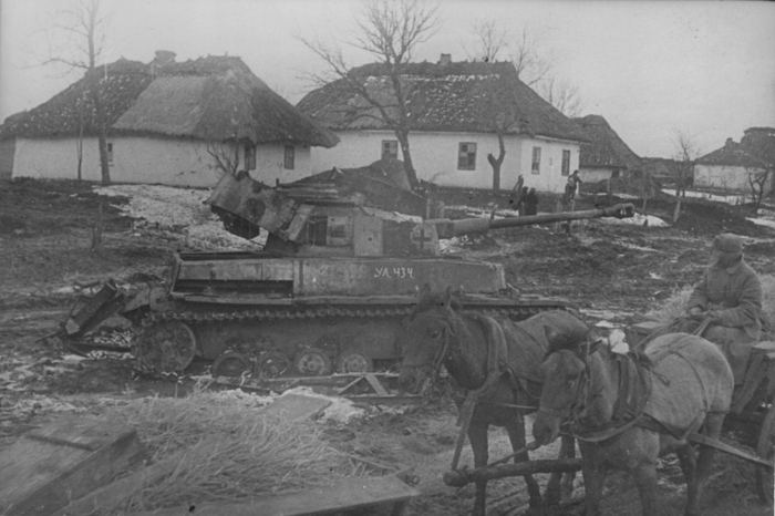 Советский солдат на конной подводе проезжает возле подбитого немецкого среднего танка Pz.Kpfw. IV в украинской деревне. На танке пометка советской трофейной команды: «УА 434». 1944